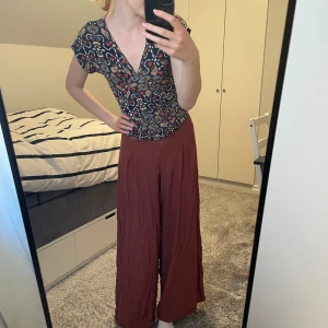 Palazzobyxor vinröd/bruna - Säljer ett par vida palazzobyxor. De är i mjukt o svalt material perfekta för sommaren🧡De blir ganska lätt skrynkliga men är i ganska bra skick annars. 