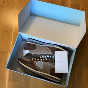 Beige och bruna sneakers från Philippe Model - Snygga sneakers från Philippe Model i en stilren kombination av beige och brunt. Skorna har en rund tå och snörning framtill. Tillverkade i mocka och skinn, vilket ger en lyxig känsla. Perfekta för en avslappnad men trendig look. Helt nya! Nypris 2800kr