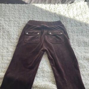 Bruna juicy mjukisbyxor med fickor  - Säljer ett par bruna mjukisbyxor med breda ben och praktiska fickor både fram och bak. Byxorna har en bekväm resårmidja med snörning för justerbar passform. Perfekta för en avslappnad stil.