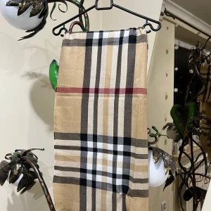 Rutig BURBERRYhalsduk - Snygg rutig halsduk i beige, svart, vit och röd. Perfekt för att ge din outfit en klassisk touch. Den har ett tidlöst mönster som passar till många olika stilar.Det ni ser på bilden är det ni får😁 ett plagg som är köpt i bulk så jag vet lila lite som ni, men jag har kollat så gott jag kan på alla möjliga sajter och det jag kan kolla stämmer överens med originalet väldigt bra tröja raka o fina sömmar, kvalitets tyg och man ser var taggen har suttit