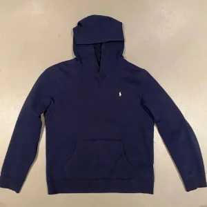 Ralph lauren hoodie - Säljer en stilren mörkblå hoodie från Ralph Lauren med en liten broderad logga på bröstet. Tröjan har en klassisk känguruficka och långa ärmar. Perfekt för en avslappnad look. Det är storlek XL i barn från kidsbrandstore men sitter som en S-XS i herrstorlek.