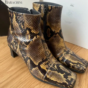 Vintage! Ormskinnsmönstrade stövletter från Luciano Barachini - Snygga stövletter i ormskinnsmönster från Luciano Barachini. De har en fyrkantig tå och en praktisk dragkedja på sidan. Klacken är låg och bekväm, perfekt för en stilren look.