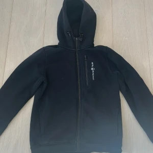 Svart huvtröja från Sail Racing - Säljer en svart sail racing hoodie med dragkedja. Storlek 160