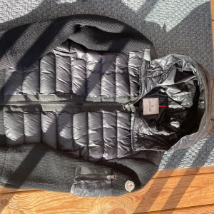Svart Moncler cardigan - Säljer en snygg svart pufferjacka från Moncler. Jackan har en quiltad design med dragkedja framtill och en huva. Perfekt för kyligare dagar med sin stilrena look och funktionella detaljer.