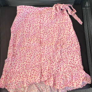 Blommig kjol från VILA - Söt blommig kjol från VILA i rosa och vit med volangdetaljer och knytband i midjan. Perfekt för en somrig look!