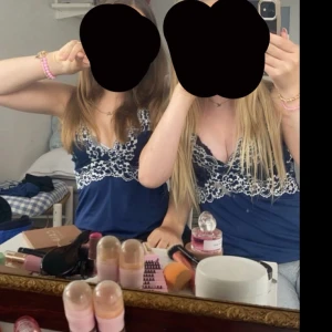 Mörkblå linne med spetsdetaljer - Snygg mörkblå linne med vita spetsdetaljer längs urringningen. Perfekt för en somrig look eller en avslappnad dag. Linnet har en elegant och feminin design.