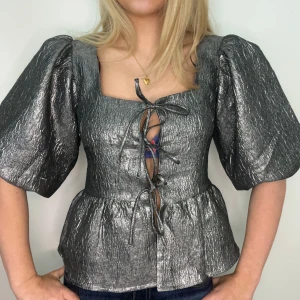 Silverglittrig topp med puffärmar - Snygg silverglittrig topp med puffiga kortärmar och knytning framtill. Perfekt för en festlig kväll!