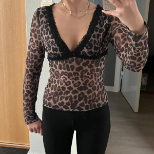 Leopardmönstrad topp med spetsdetaljer - Snygg leopardmönstrad topp med djup v-ringning och svarta spetsdetaljer. Toppen har långa ärmar och en tight passform, perfekt för en trendig look. Knappt använd, mycket fint skick!