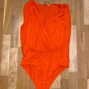 Orange omlott body - Säljer en snygg orange omlott body med v-ringning. Perfekt för att ge en färgklick till din outfit. Den är ärmlös och har en bekväm passform.