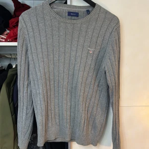Grå ribbad tröja från GANT - Säljer en stilren grå ribbad tröja från GANT. Tröjan har en rund halsringning och långa ärmar. Perfekt för en avslappnad och snygg look. Passar bra till både jeans och chinos.