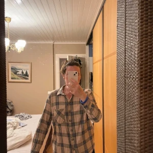 Beige rutig skjorta från H&M Divided - Säljer en beige rutig skjorta från H&M Divided. Skjortan har långa ärmar och knappar framtill. Den har en klassisk krage och en bröstficka. Perfekt för en avslappnad stil.