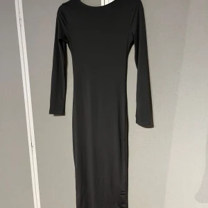 Grå långklänning från Venderby's - Elegant grå långklänning från Venderby's med långärmad design och öppen i ryggen. Klänningen får ej längre att få tag i och går ner till vaderna 