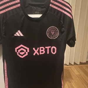 Inter Miami tröja - Säljer en Inter Miami tröja med Messis namn på ryggen. Tröjan har korta ärmar och klubbmärke på bröstet. Messi och nummer 10 är tryckt på baksidan. Perfekt för fans av laget!