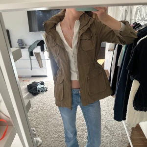 Militärgrön jacka från H&M - Säljer en mörkgrön jacka från H&M med dragkedja och inzippbar luva i nacken. Jackan har en normal passform och är perfekt för höst och vår. Den har långa ärmar och en justerbar midja för bättre passform. 🩷 står ej för postens slarv eller frakt!!
