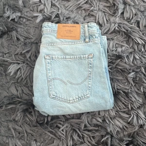 Ljusblå jeans från Jack & Jones - Snygga ljusblå jeans från Jack & Jones med klassisk femficksdesign och knappgylf. Hål på knäna och är lite loose. Märkeslapp i läder baktill ger en extra touch.