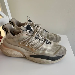 Beige sneakers från Adidas - Säljer ett par beige sneakers från Adidas med svarta och vita detaljer. Skorna har en chunky sula och snörning framtill. Perfekta för en sportig look.