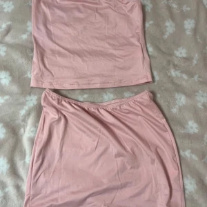 Rosa set med tubtopp och kjol - Säljer ett sött rosa set bestående av en tubtopp och en matchande kortkjol. Perfekt för varma dagar eller sommarens fester. Setet är gjort i ett mjukt och bekvämt material. Aldrig använd.