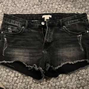 Svarta jeansshorts med fransar - Snygga svarta jeansshorts med fransiga kanter och slitna detaljer. De har en knapp och dragkedja framtill samt fickor både fram och bak.midjemåttet är 40