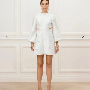 Vit klänning med öppen rygg By Malina - Elegant vit klänning med lång puffärm och öppen rygg från By Malina. Klänningen har en kort längd och ett subtilt blommigt mönster. Perfekt för studenten. Nypris 5000kr