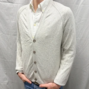 Topman ljusgrå kofta med knappar - Säljer en stilren ljusgrå kofta från Topman med knappar framtill. Koftan har långa ärmar och en klassisk design som passar perfekt till både skjorta och t-shirt. Perfekt för en avslappnad men ändå uppklädd look. Bra skick, inga defekter. Modellen är 182cm/ 67kg 