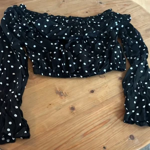 Svart prickig offshoulder blus - Säljer en söt svart offshoulder blus med vita prickar. Blusen har långa ärmar och en elastisk kant vid axlar och midja för en bekväm passform. 