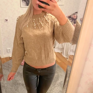 Beige stickad tröja med pärlor - Snygg beige stickad tröja med pärlor runt halsen. Tröjan har långa ärmar och ribbade muddar vid ärmslut och nederkant💗💗