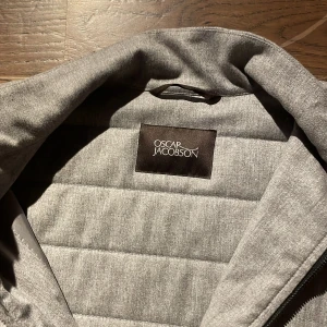 Grå quiltad väst från Oscar Jacobson - Snygg grå quiltad väst från Oscar Jacobson med dragkedja framtill. Perfekt för lager-på-lager under kyligare dagar eller nu till våren. Stilren design som passar till många olika outfits. Nypris 3000kr mitt pris 900kr pris kan självklart diskuteras . Är som helt ny utan några defekter. Storlek M men passar även S