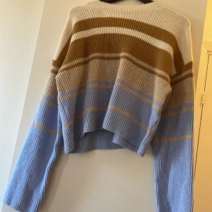 Randig stickad tröja i blått och brunt - Säljer en mysig stickad tröja med randigt mönster i blått, brunt och vitt. Tröjan har långa ärmar och en croppad passform, perfekt för kyliga dagar. Den ribbade strukturen ger en extra touch av stil. Perfekt för höst och vinter!