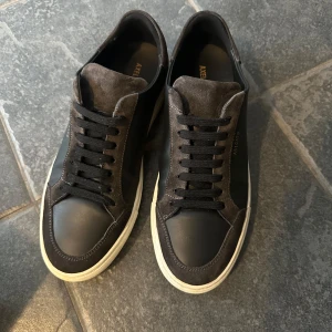 Svarta sneakers från Axel Arigato - Snygga svarta sneakers från Axel Arigato med en stilren design. Skorna har en kombination av skinn och mocka med svarta snören och en vit sula. Perfekta för en casual look.nypris 2700kr 