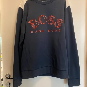 Mörkblå sweatshirt från Hugo Boss - Snygg mörkblå sweatshirt från Hugo Boss med röd broderad logga på bröstet. Tröjan har långa ärmar och en rund halsringning. Perfekt för en stilren och avslappnad look. Den är helt ny från Hugo boss i storlek XS