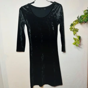 Sofistikerad svart sammetsklänning – elegant, figurnära & tidlös Nyskick  - Stilren och elegant svart sammetsklänning med rundad urringning och långa ärmar. Stretchigt material som sitter bekvämt och smickrande. Perfekt för både vardag och fest! I mycket fint skick utan skavanker. Längd 82 cm, midja 70 cm (mätt i plant läge).  Jag erbjuder bundle-rabatt vid köp av flera plagg!  