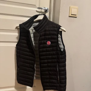 Svart dunväst från Colmar - Snygg svart dunväst från Colmar. Har använts fåtal gånger därför är den i väldigt fint skick. Det är storlek 48 vilket även passar S. Säljer pga för liten. För fler frågor kontakta mig.