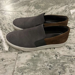 Lanvin loafers  - Snygga loafers från Lanvin i en stilren kombination av grått och brunt. Skorna har en slät ovandel med elastiska paneler för enkel på- och avtagning. Perfekta för en avslappnad och soft look. Storlek 43