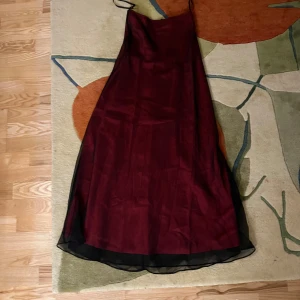 Vinröd maxikjol  från Faviana - Elegant vinröd maxikjol från Faviana . Perfekt för festliga tillfällen. Kjolen har en mörk underton och är  lätt utsvängd.