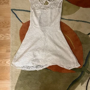 Vit spetsklänning från Voir - Säljer en söt vit spetsklänning från Voir i storlek XS. Klänningen har en kort längd och är ärmlös med ett fint spetsmönster. Perfekt för sommarens alla tillfällen eller kanske till studenten 