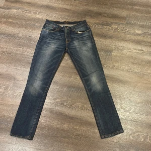 Mörkblå jeans från Nudie Jeans W33 L34 - Snygga mörkblå jeans från Nudie Jeans med en klassisk straight passform. De har en lätt slitning på framsidan och bakfickor med dekorativa sömmar. Perfekta för en avslappnad stil. 