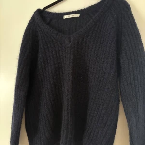 Mörkblå stickad tröja från Gestuz - Säljer en mysig mörkblå stickad tröja från Gestuz. Tröjan har en v-ringad design och långa ärmar, perfekt för kyliga dagar. Den ribbade strukturen ger en stilren look. Passar utmärkt till både jeans och kjol. Nästan aldrig använd 