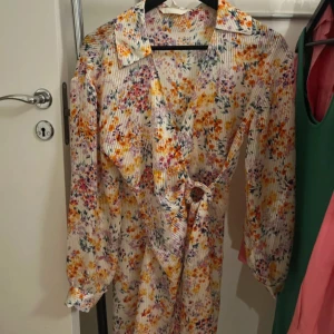 Blommig omlottklänning med knytning  - Säljer en vacker blommig omlottklänning med knytning i midjan och långa armar☀️