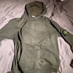 Stone island hoodie - En riktigt snygg Stone Island hoodie i en grön färg. Hoodien är använd en del men är fortfarande i bra skick. Tyvärr har jag dock råckat tvätta tröjan med märket på och detta har lätt till att märket blivit skrynkligt o missformat. Där av det lägre priset. Inget som synns vid användning men man kan även köpa till märken på annat håll om det nu är så att man vill ha ett nytt. Storlek M. Kom privat vid fler frågor!