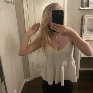 Vit ärmlös topp - INTRESSEKOLL!! Säljer en stilren vit ärmlös topp med smala axelband och en luftig passform. Toppen har en volangdetalj vid nederkanten som ger en touch. Perfekt för varma dagar eller sommarens fester.🩷🩷