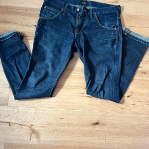 Blå jeans från Lee W/32 L/34  - Snygga blå jeans från Lee med klassisk femficksdesign och knappgylf. Jeansen har en rak passform och är perfekta för en avslappnad stil. De har en mörkblå tvätt och är tillverkade i slitstarkt denim.