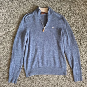 Blå merinoulltröja från Morris - Säljer en stilren blå tröja från Morris i 100% merinoull. Tröjan har en dragkedja vid halsen och ett litet broderat emblem på bröstet. Aldrig använd. Nypris:1800kr, mitt pris 550