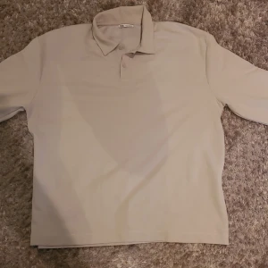 Ljusgrå pikétröja från Zara - Säljer en stilren beige pikétröja från Zara. Tröjan har en klassisk krage och knappar framtill. Perfekt för en avslappnad men ändå snygg look.