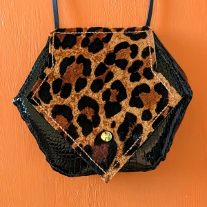 Svart axelväska med leoparddetaljer - Unik svart axelväska i syntet med krokodilmönster och leoparddetaljer. Väskan har en iögonfallande design med en leopardmönstrad ficka framtill och en praktisk dragkedja. Perfekt för att ge din outfit en djärv touch.