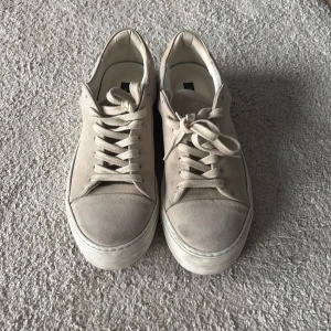Beige sneakers från Sneaky Steve - Snygga beige sneakers från Sneaky Steve med snörning och en stilren design. Skorna har en tjock sula och är tillverkade i mocka, vilket ger dem en lyxig känsla. Perfekta för en avslappnad och trendig look.