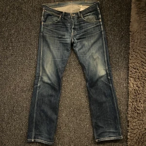 Blå jeans från Wrangler - Snygga blå jeans från Wrangler med klassisk femficksdesign och märkets ikoniska W-söm på bakfickorna. Jeansen har en normal passform och är tillverkade i slitstarkt denim. Perfekta för en avslappnad stil. Lite slitna, säljer pga att dem var lite stora i midjan, då stroleken var 32L och 32w och jag brukar ha 30w.