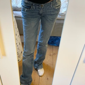 Lowwaist jeans/dżinsy z niskim stanem - Snygga blå jeans från LA Company med en unik broderad design på bakfickan. De har en låg midja och en bootcut-stil som ger en avslappnad look. Midjemått rakt över: 37 cm. Innerbenslängd: 83 cm.