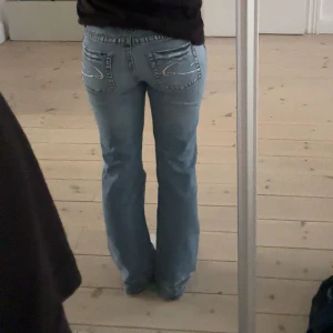 Ljusblå jeans med broderade bakfickor - Snygga ljusa jeans med broderade detaljer på bakfickorna. De har en låg midja och en bootcut-stil som ger en avslappnad look. Perfekta för en casual outfit. Mått: 38 cm & 80 cm