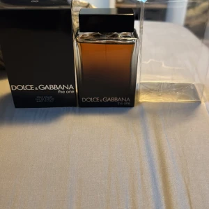 Dolce & Gabbana The One EDP 150ml - Säljer en lyxig herrparfym från Dolce & Gabbana, The One. Flaskan är elegant med en mörk bärnstensfärg och svart lock. Innehåller 150 ml av en förförisk doft som kombinerar orientaliska och kryddiga toner. Perfekt för den som vill ha en sofistikerad och tidlös doft.