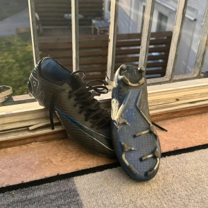 Nike Mercurial  - Säljer ett par svarta fotbollsskor från Nike med vita och blåa detaljer. Skorna har snörning och är designade för optimal prestanda på planen. Perfekta för fotbollsspelare som vill ha stil och funktionalitet. Skick 7/10 Strlk 40
